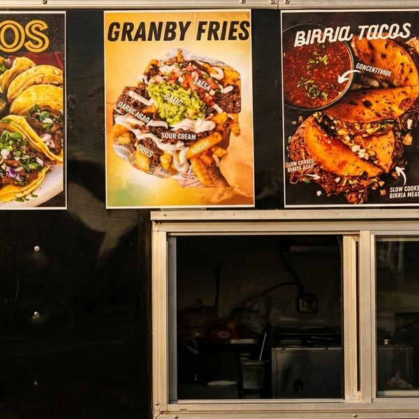 Food truck menu posters display tacos, Granby fries, and birria tacos above a service window.