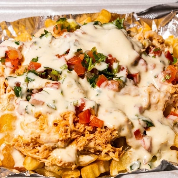 Loaded fries with shredded chicken, melted cheese, and pico de gallo in a takeout container.